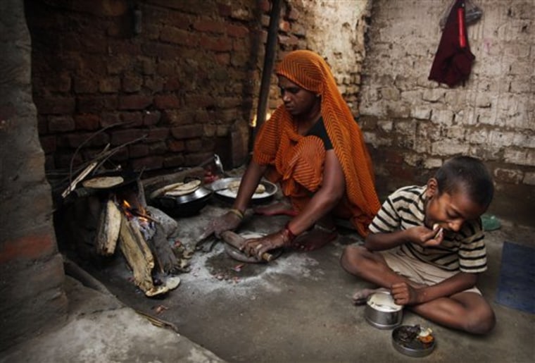 In this Saturday, Oct. 23, 2010 picture, a woman prepares chapati, a traditional bread made with wheat flour, by the fireside as her son eats a meal at their home in Allahabad, India. Agronomists say rising temperatures from global warming are reducing India's wheat crop. Scientists say future global wheat supplies are in question because of stagnating yields, the spread of a devastating wheat fungus, climate change and a volatile, unreliable market. (AP Photo/Rajesh Kumar Singh)